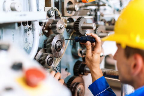 Instandhaltung Werker mit Helm schraubt an einer Industriemaschine